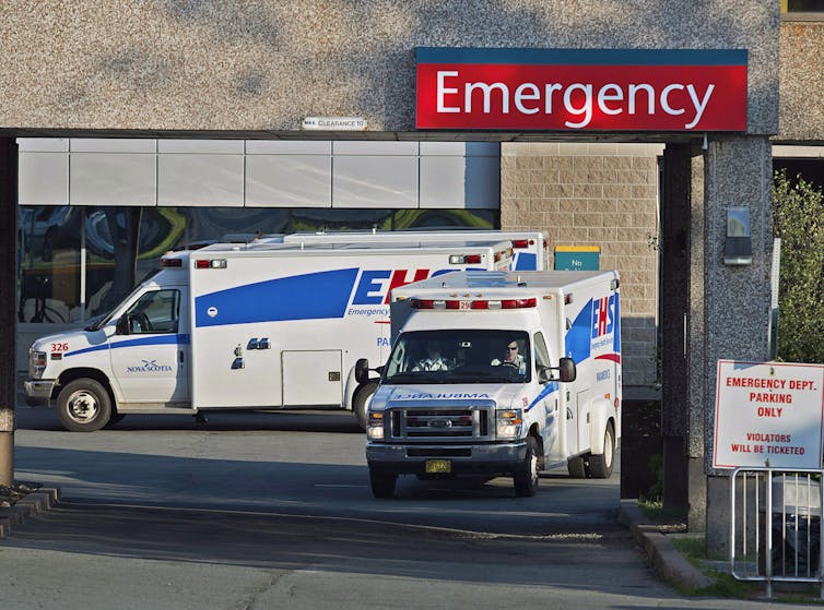 Two ambulances under a large red emergency sign.