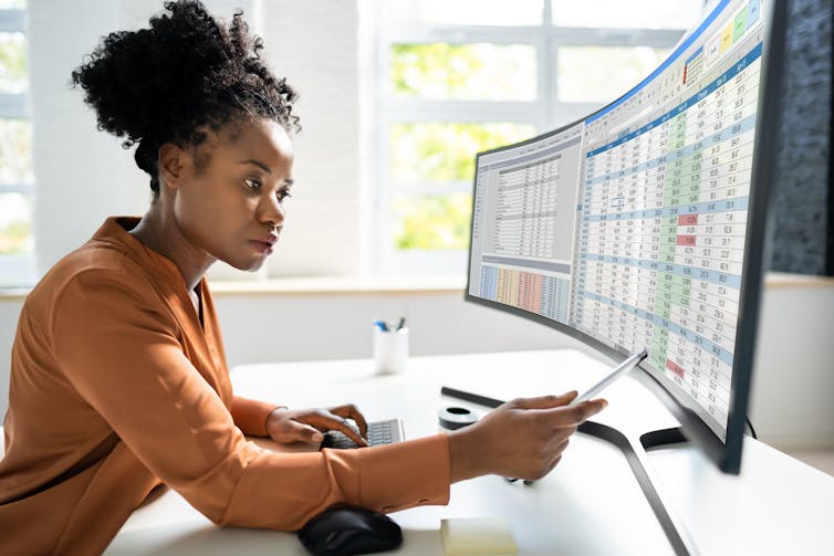 A woman pointing her pen at a spreadsheet displayed on her computer monitor.