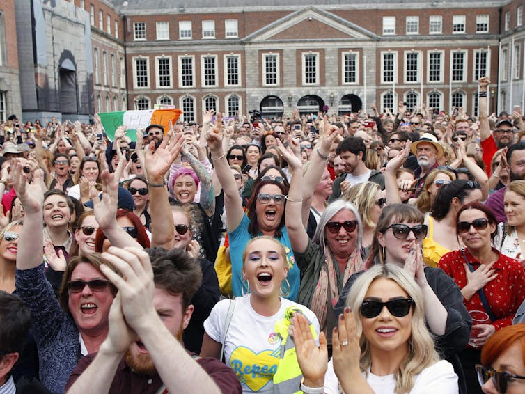 Hundreds of women cheer outside a stone building.