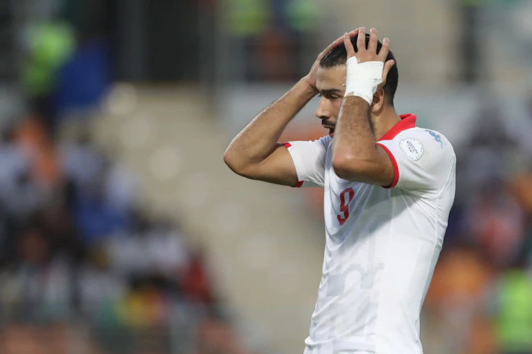 A man in football gear holds his head, his mouth open in shock.