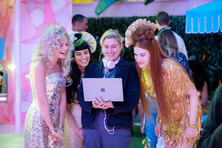Director Greta Gerwig on the set of Barbie looking at a screen and surrounded by actors.
