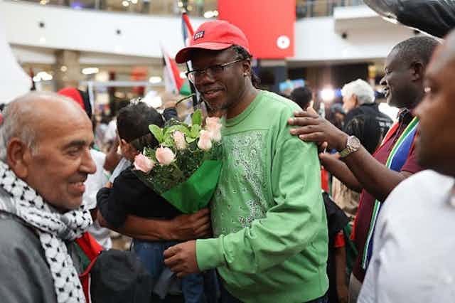 Un homme tient un bouquet de fleurs tandis que les gens autour de lui sourient.