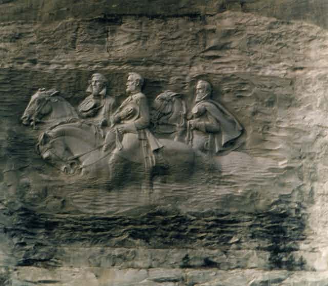A stone carving shows three white men are riding on horses.