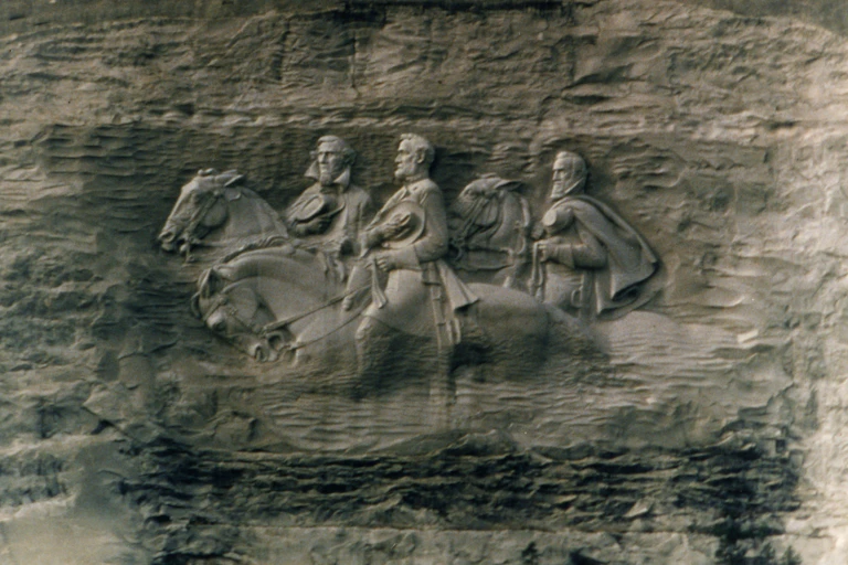 A stone carving shows three white men are riding on horses.