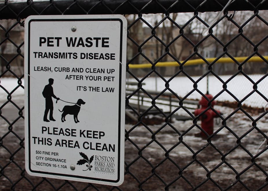 a sign on a fence warns 'Pet waste transmits disease' with dog park in background