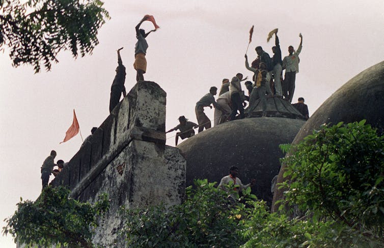 Hindu worshippers stand above the top dome of an ancient mosque waving saffron flags.