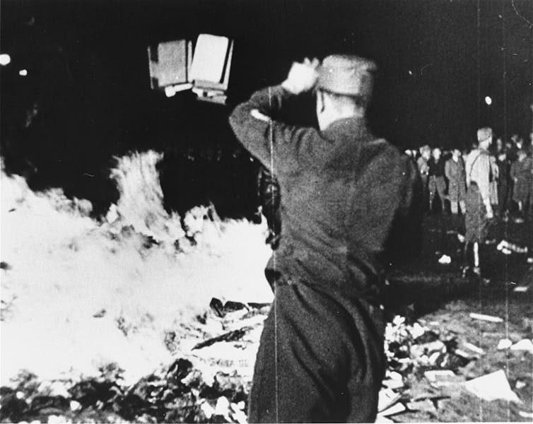 Black and white photo of person in uniform throwing books into a bonfire