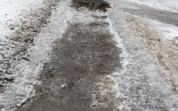 A snowy sidewalk covered in tiny chunks of salt.