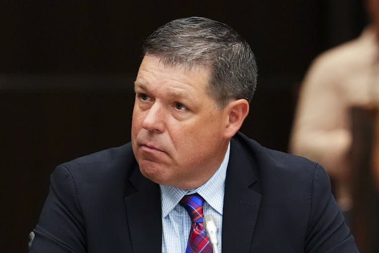 A headshot of a middle-aged white man in a suit