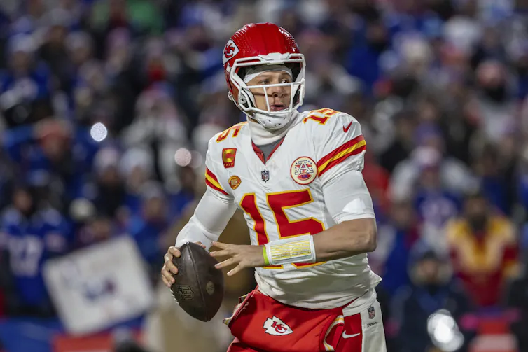 A football player holds a football between his hands as he looks off to the side