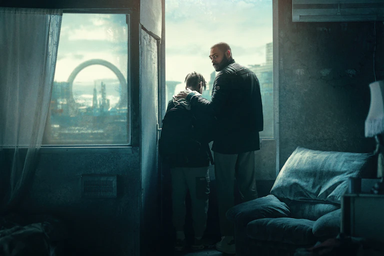Two people in an interior with a view over a city.