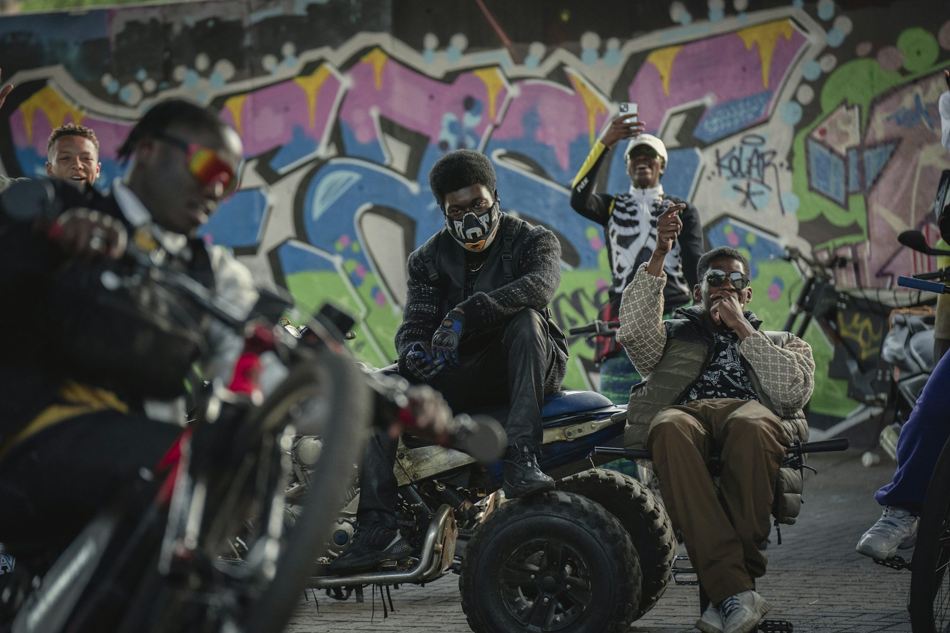 Men on bikes in front of a graffitied wall.