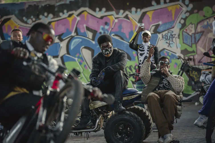 Men on bikes in front of a graffitied wall.