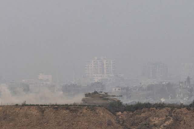 A tank rides along the northern border of Israel. Smoke billows in the background.