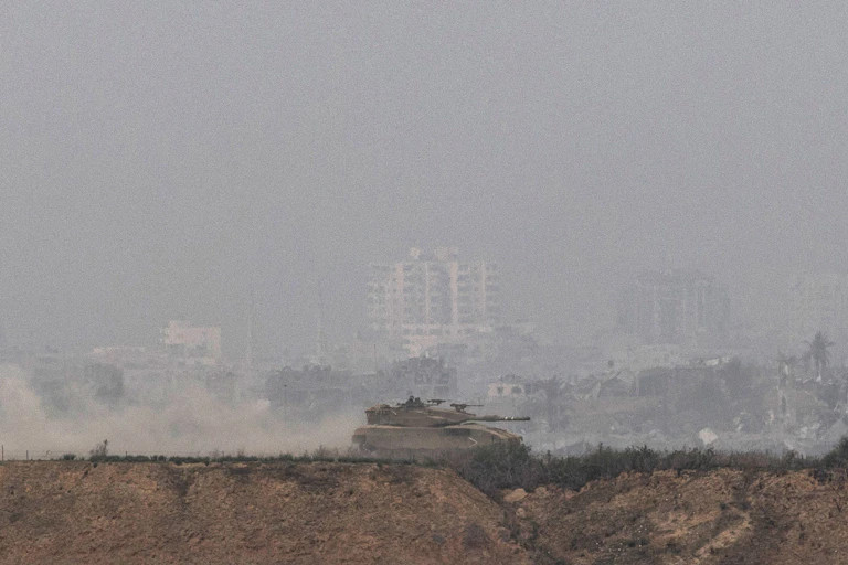 A tank rides along the northern border of Israel. Smoke billows in the background.