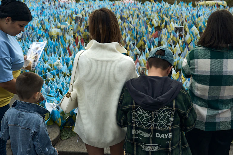 Women and children stand looking at blue and yellow flags.