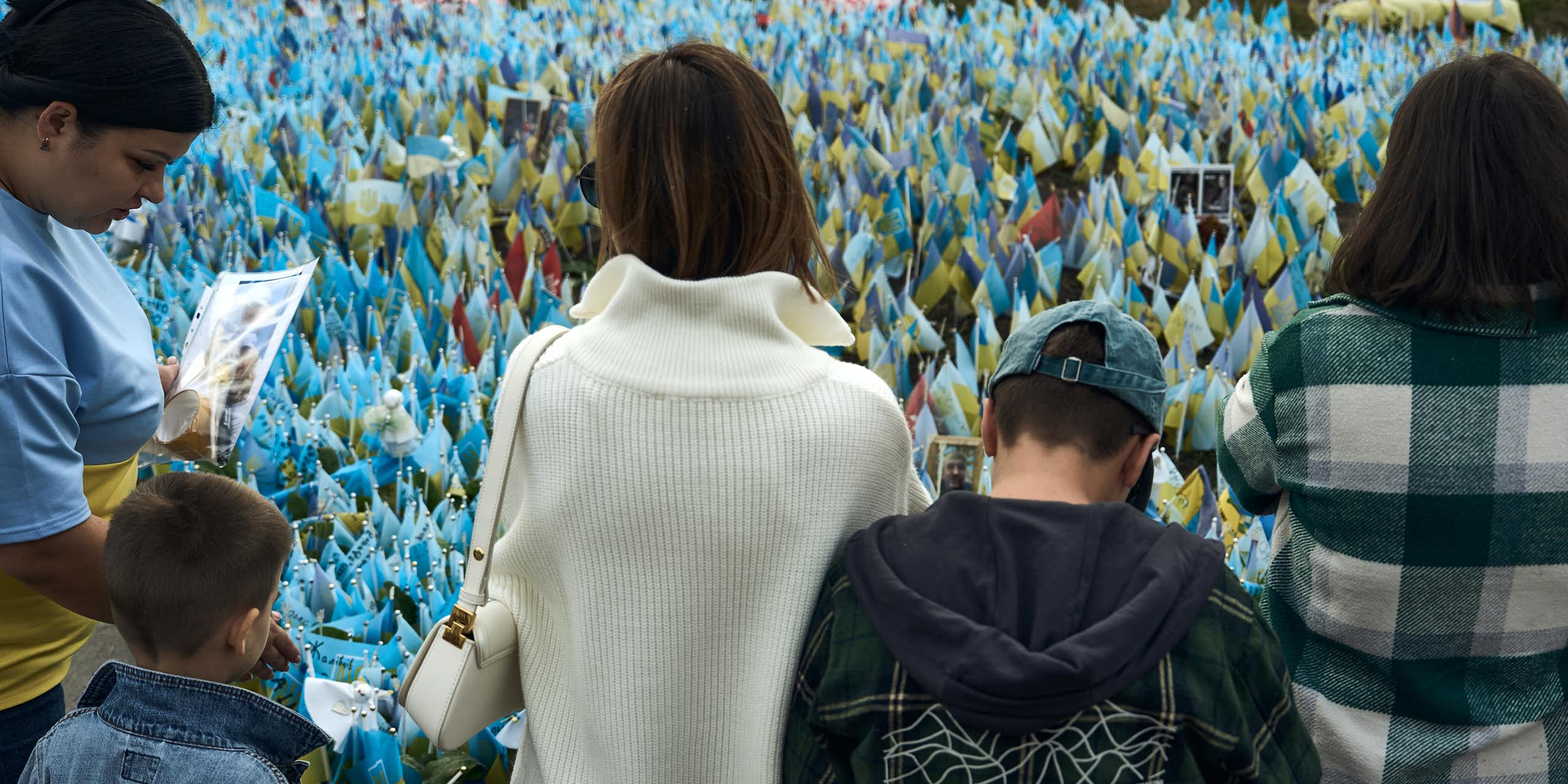 Women and children stand looking at blue and yellow flags.