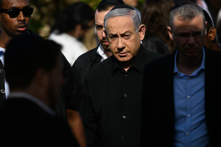 Benjamin Netanyahu wears a black button down shirt and a black kippah and stands in a group of other men.