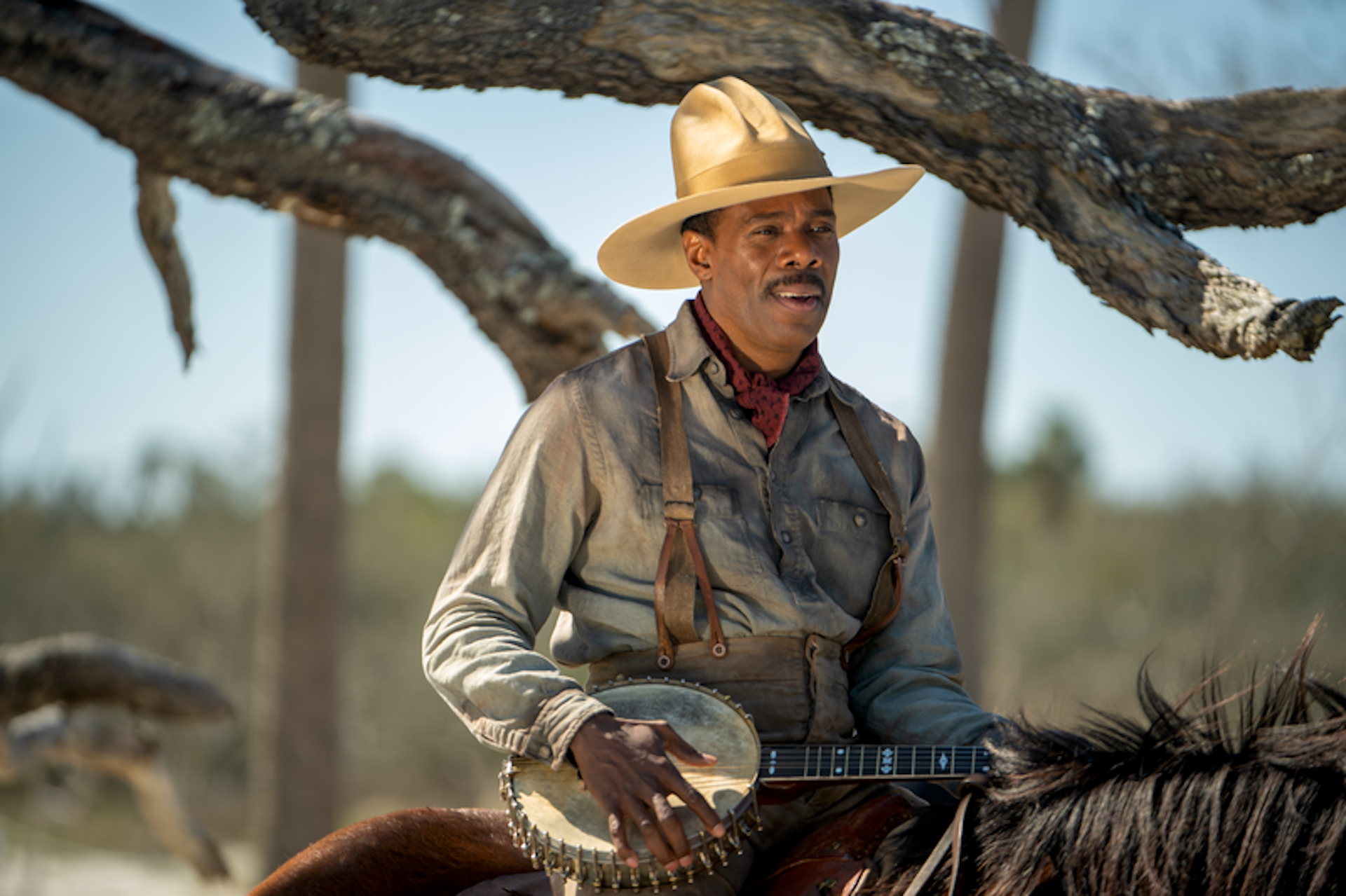Mister, wearing a straw hat and playing a banjo while riding a horse