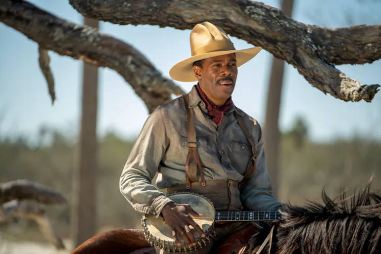 Mister, wearing a straw hat and playing a banjo while riding a horse