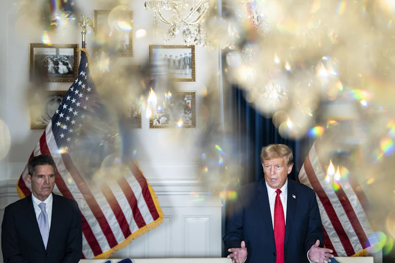 Two men talking in a room behind a chandelier.