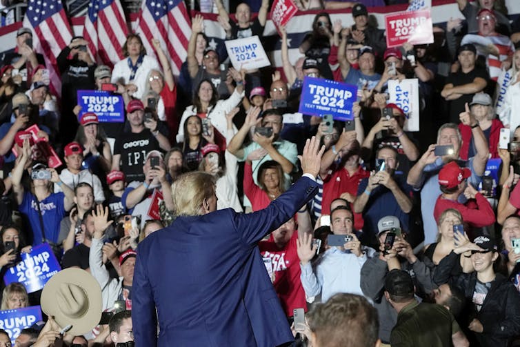 A man stands waving to a crowd of people holding signs.