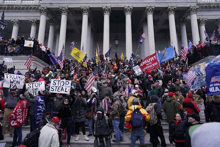 A crowd with banners and flags climbing stairs of large government building with white columns.