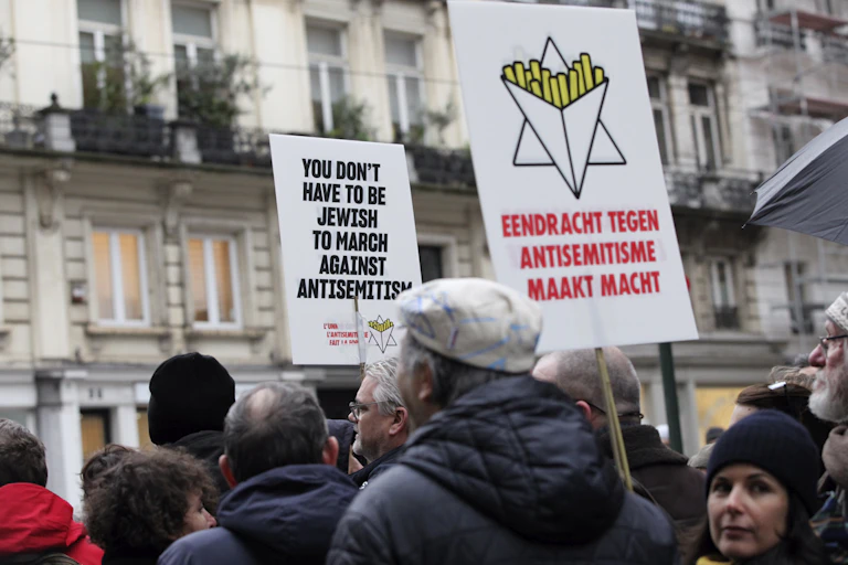 Several people marching in a protest holding placards, one of which reads, You don't have to be Jewish to march against antisemitism.'