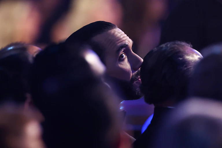 A man in a beard looks over his shoulder above the heads of others.