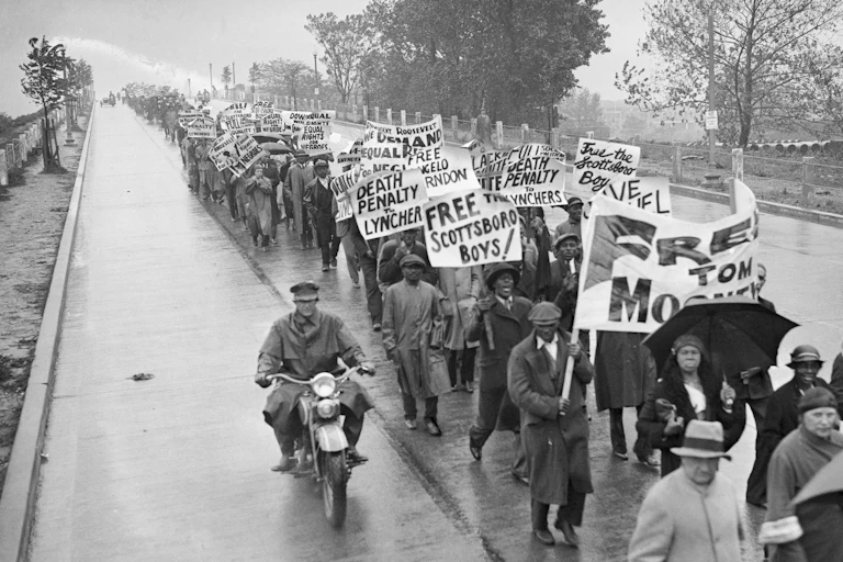 Hundreds of Black men and women are carrying large posters as they march in the rain.