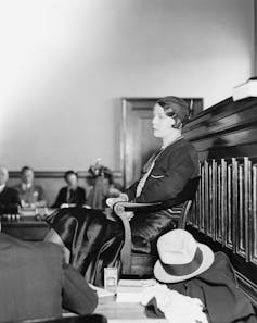 A white woman is sitting on a chair as she answers questions.