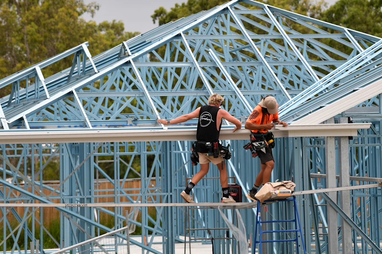 Two workman standing on scaffolding as they install a gutter on a new house