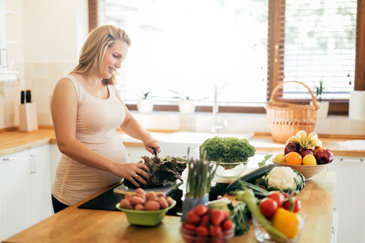 A pregnant woman preparing vegetables in the kitchen.