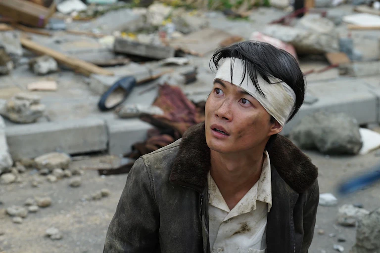 Production still: a man on a destroyed road