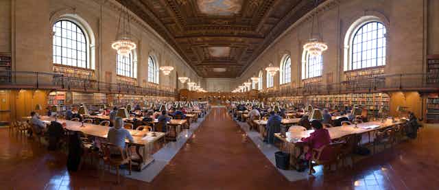 Panoramic view of library reading room with patrons seated at rows of desks.