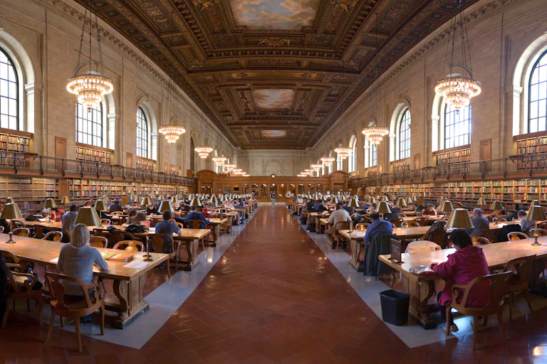 Panoramic view of library reading room with patrons seated at rows of desks.