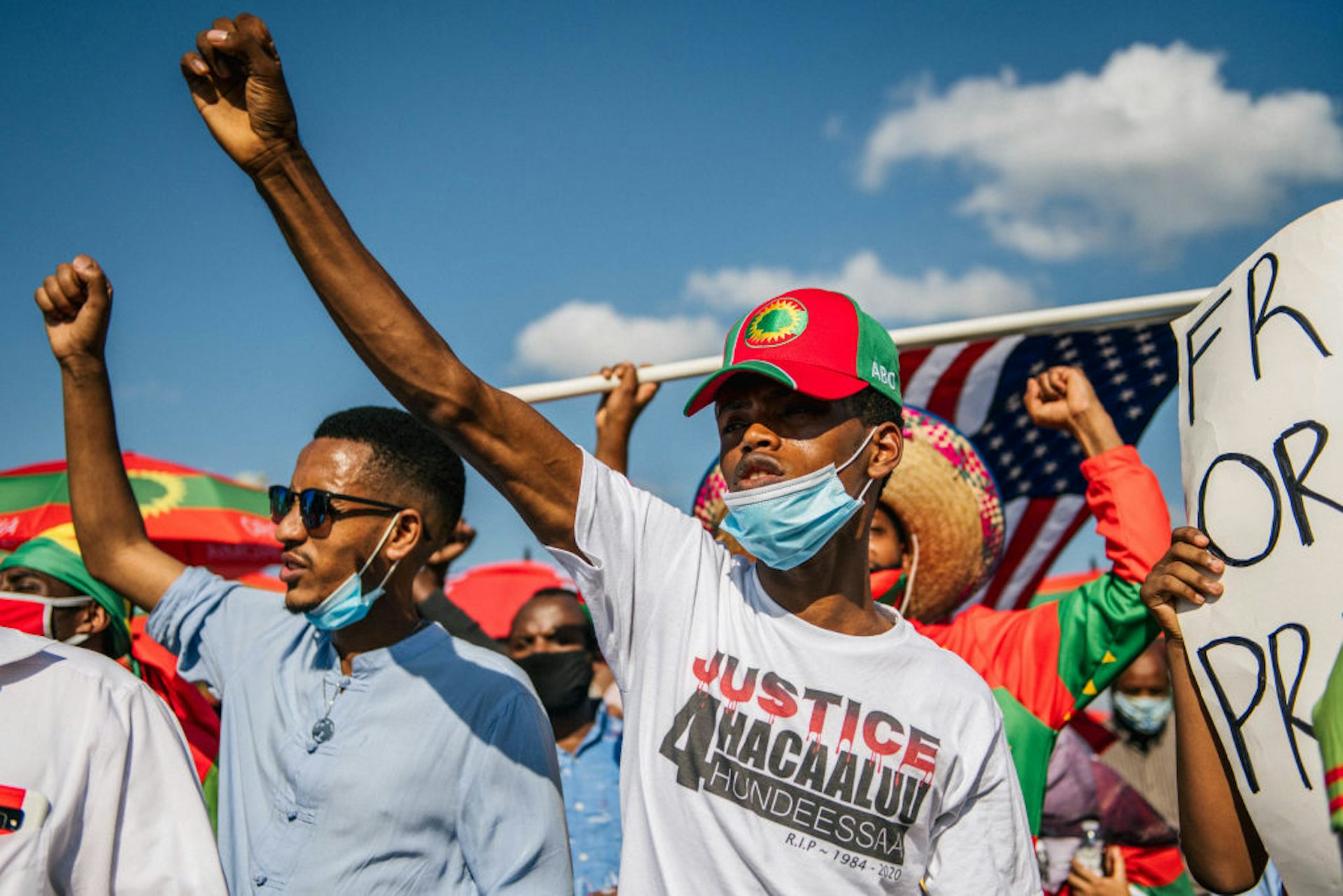 A group of men, several carrying banners and one wearing a t-shirt that calls for justice for Hachalu Hundessa, raise their fists in the air
