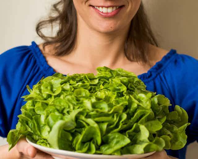 Woman in blue top holds a shallow bowl filled with leafy green salad