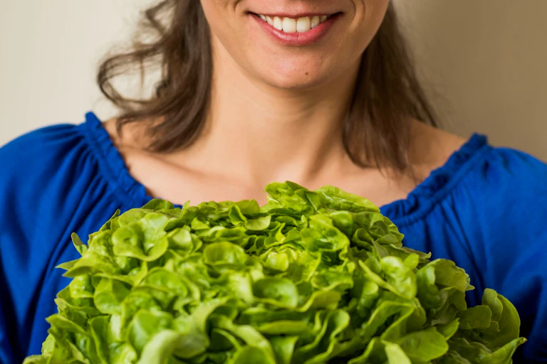 Woman in blue top holds a shallow bowl filled with leafy green salad
