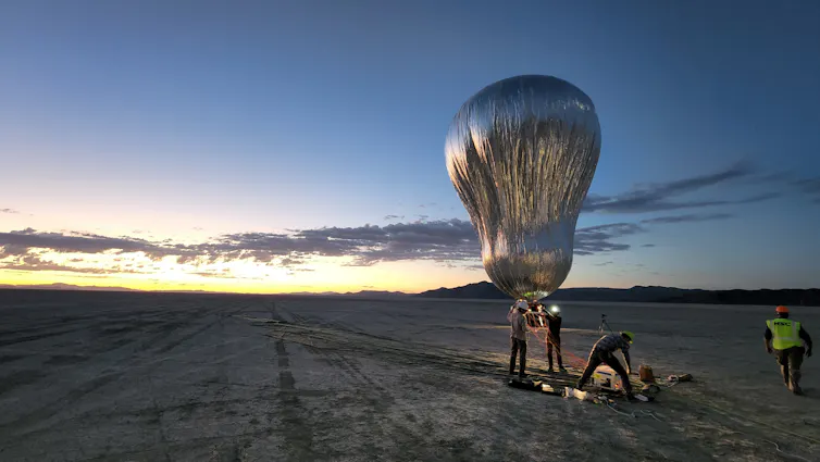 Grande balão prateado sendo lançado no deserto.