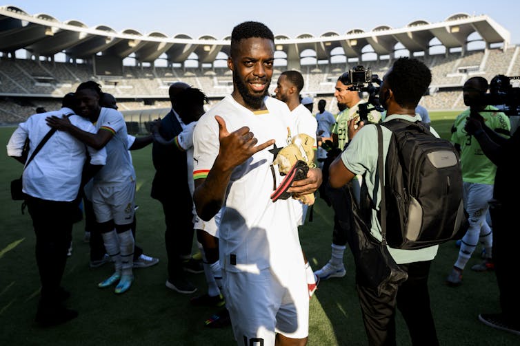 A Ghanaian soccer player on the field looks straight into the camera celebrating.