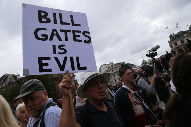 Man at protest holds sign reading "Bill Gates is evil"