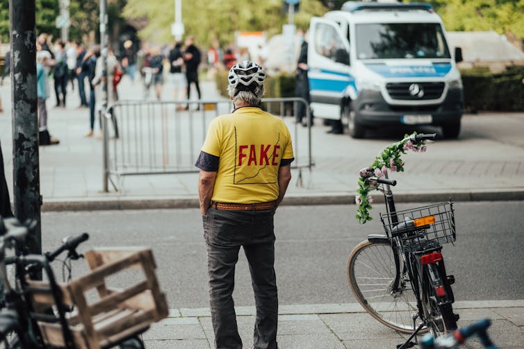 Homem protestando sozinho usando camisa amarela com gráfico e a palavra falso
