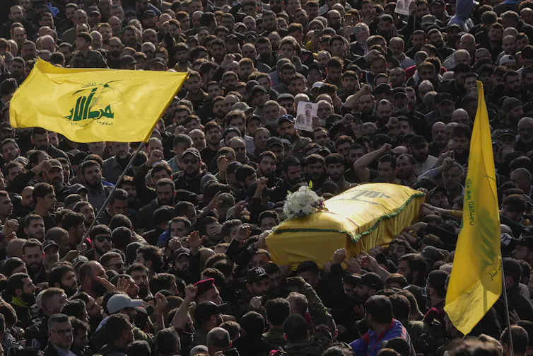 A sea of people carry a casket draped in a yellow flag.
