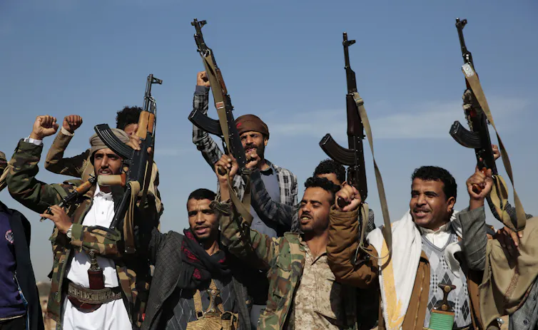 Men hold assault rifles over their heads, some with raised fists.