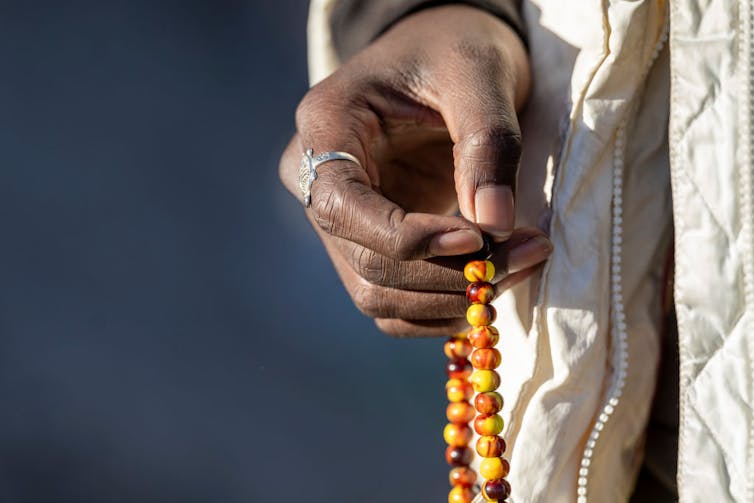 The hand of someone wearing a white coat and a silver ring holds an orange and brown string of beads.