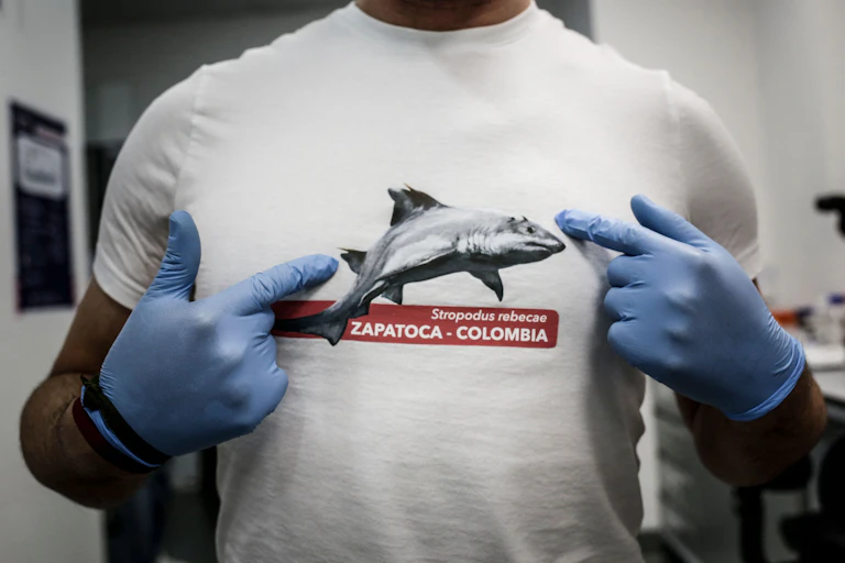 A man wearing lab gloves points to a shark image on his shirt