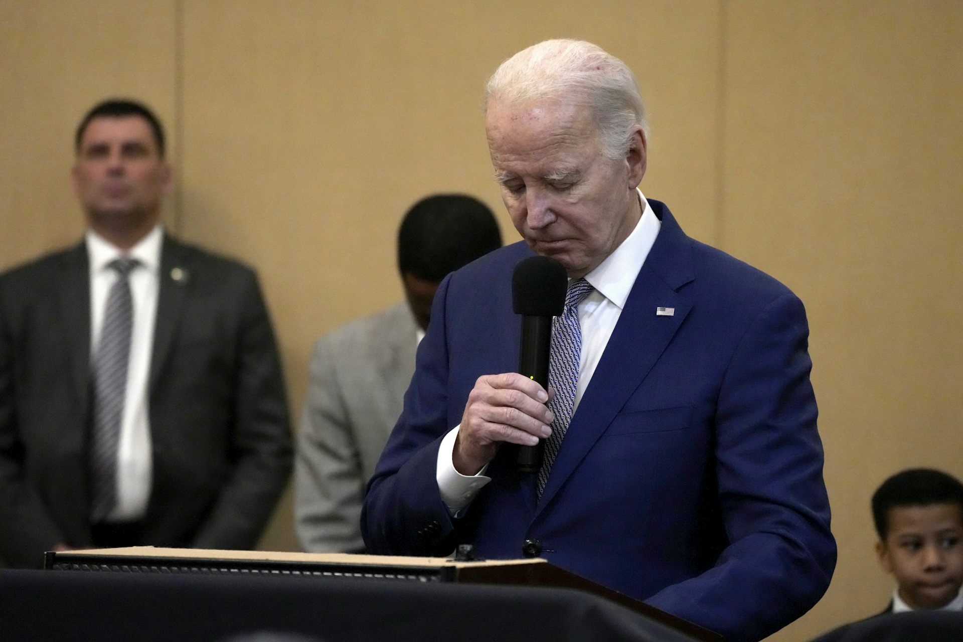 A man in a blue suit bows his head while holding a microphone.