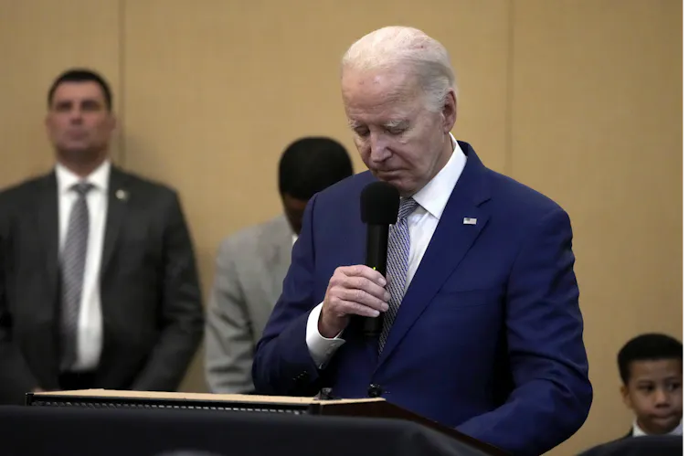 A man in a blue suit bows his head while holding a microphone.