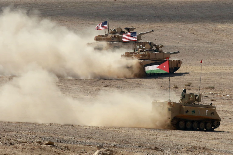 Tanks with Jordanian and US flags drive through the desert, kicking up dust.